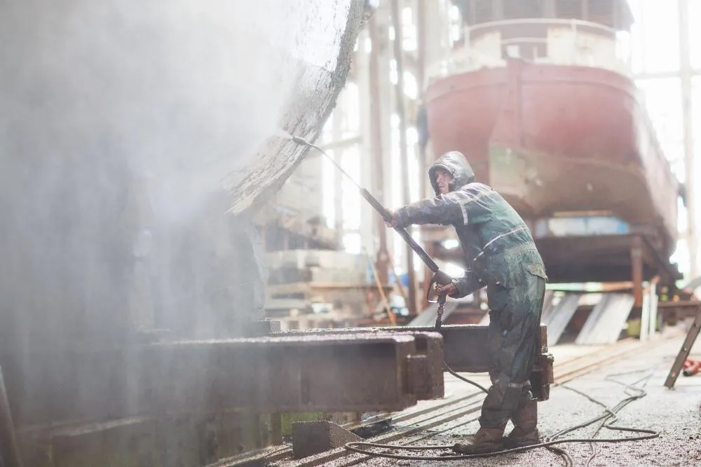 Worker Using High Pressure Hose On Boat In Shipyard