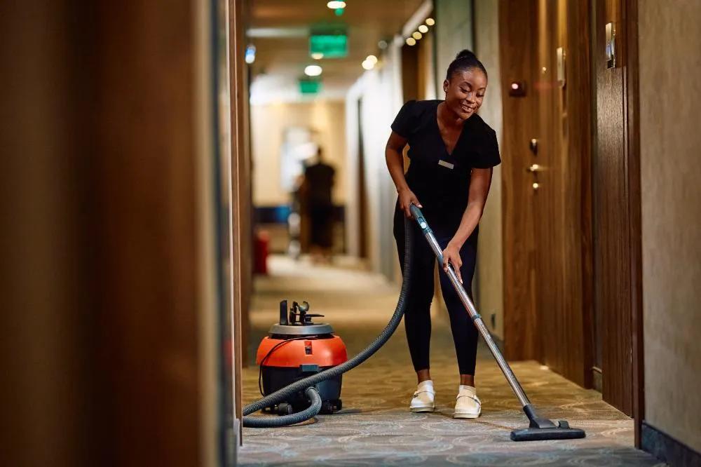Young Black Maid Vacuuming Hallway While Working